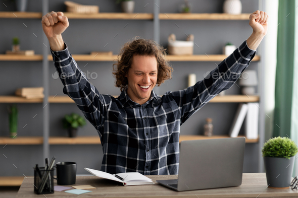 Joyful Young Businessman At Laptop Shaking Fists Sitting In Office
