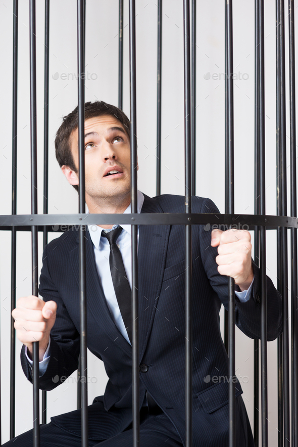 I am not guilty! Terrified young man in formalwear standing behind a prison cell and looking up