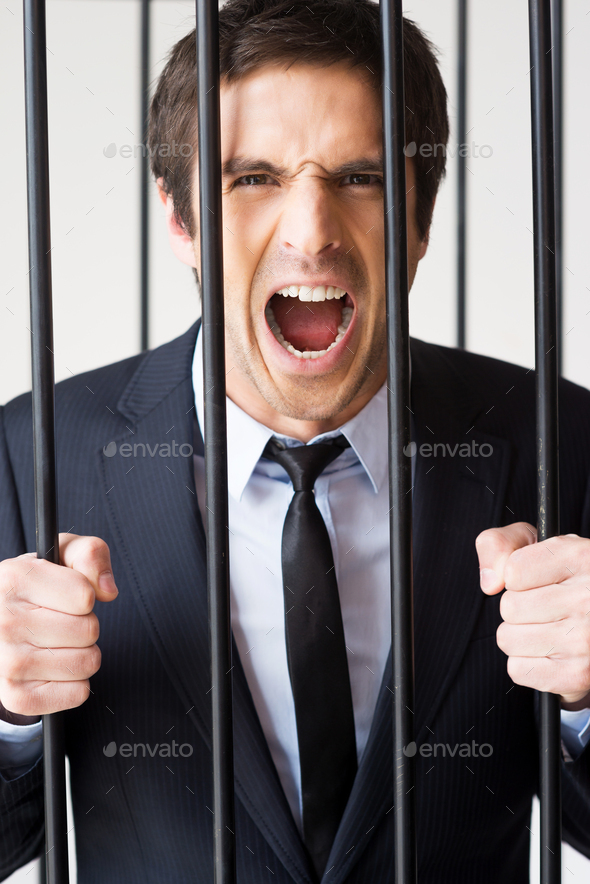 I am not guilty! Furious young man in formalwear standing behind a prison cell and shouting