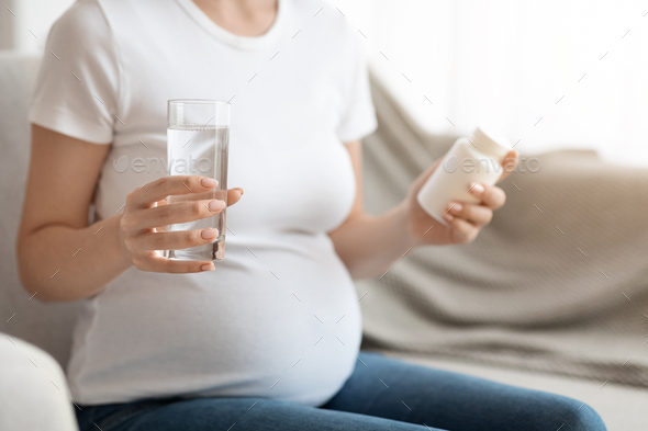 Pregnant Woman Holding Jar With Prenatal Vitamins And Glass Of Water, Cropped