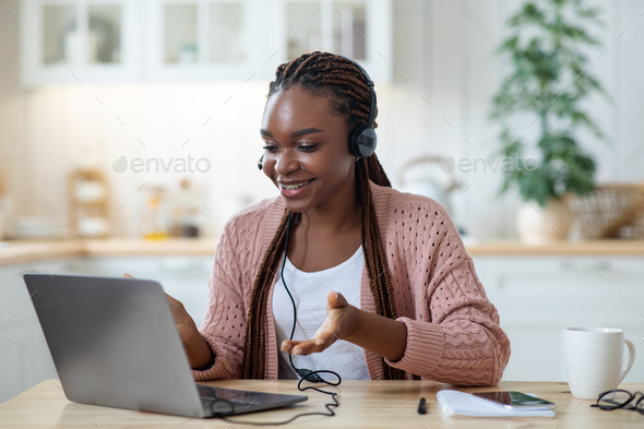 Online Tutoring. Smiling black female tutor in headset using laptop in kitchen
