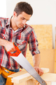 Handyman using saw. Young handyman using saw in workshop - PhotoDune Item for Sale