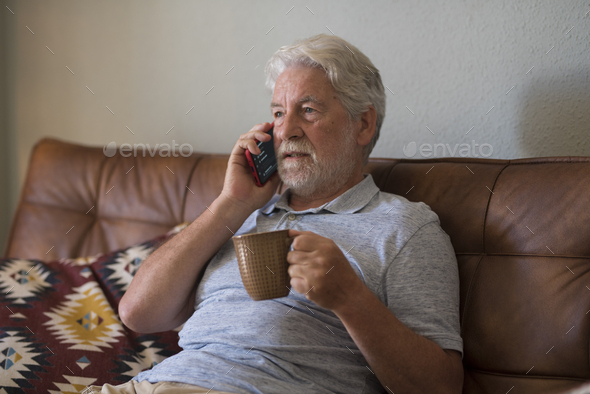 Serious senior aged man doing phone call sitting at home with smart phone - sad emotion - Stock Photo - Images