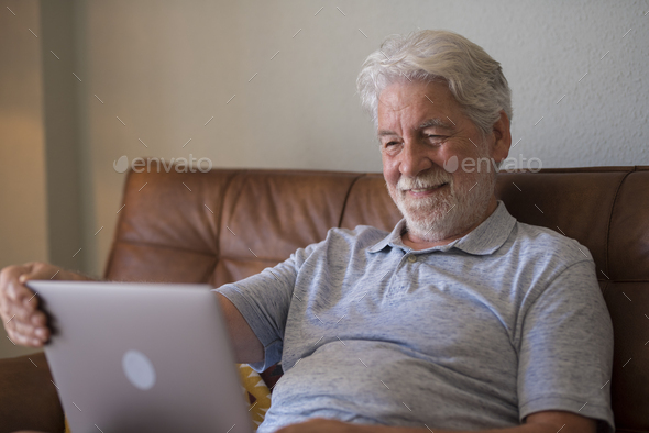 Happy aged man indoor working at laptop and smiling, relaxed senior male using computer