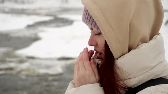 A Tourist Girl in a Beige Jacket with Red Hair Stands in the Winter Mountains