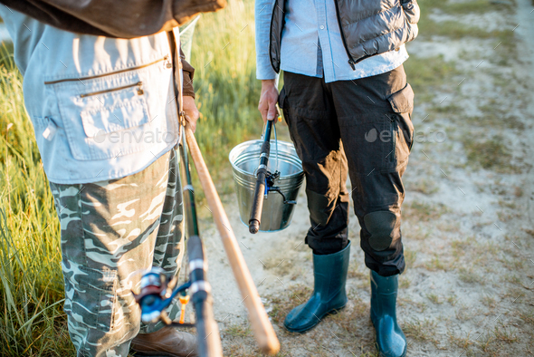 Holding fishing rods and bucket with fish outdoors Stock Photo by RossHelen