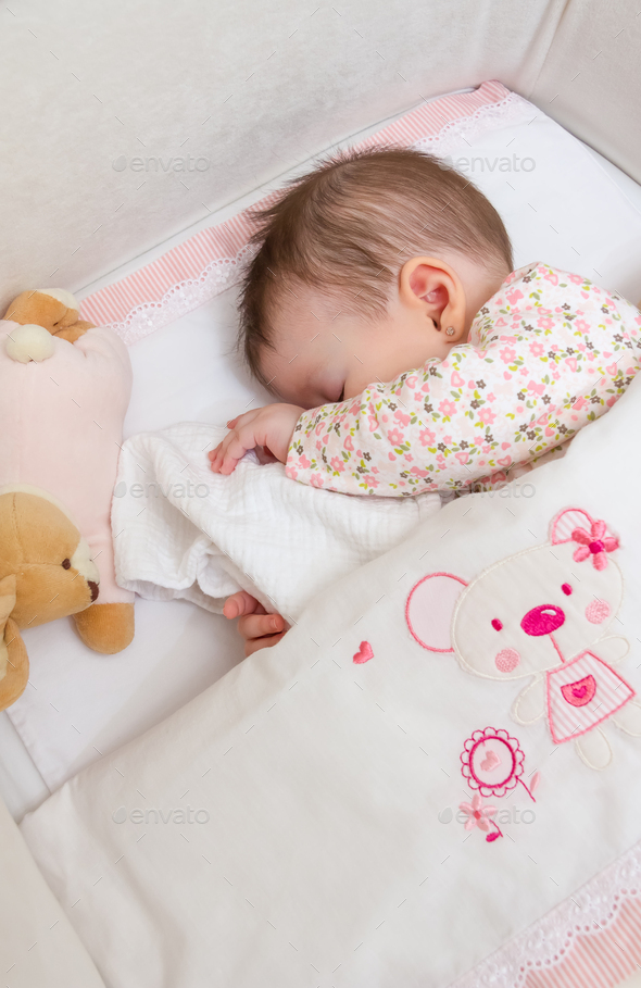 Baby girl sleeping in a cot with pacifier and toy Stock Photo by