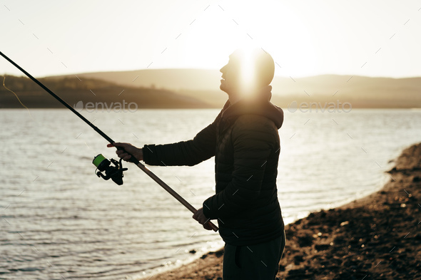 Fishing with Fishing Rod Standing on Shore of Lake Stock Photo