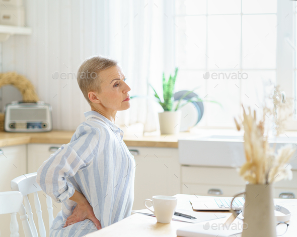 Mature woman massaging her back while working or studying on laptop online at home - Stock Photo - Images