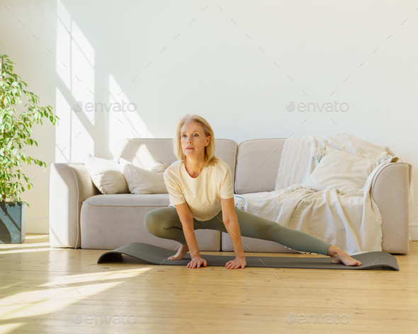 Healthy active retired woman in sportswear doing stretching exercises in on yoga mat in living room - Stock Photo - Images
