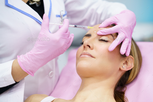 Aesthetic doctor injecting botox into the forehead of her middle-aged patient - Stock Photo - Images