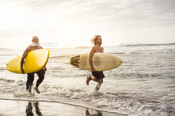 Father and son surfers run along the beach with longboards - Focus on senior\'s board