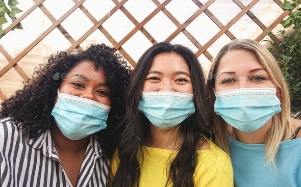 Portrait of multiracial friends wearing protective face mask outdoors - Focus on faces