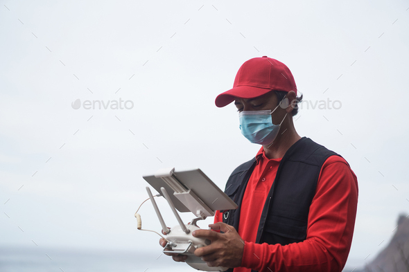 Courier man flying box for delivery with drone while wearing safety mask - Focus on face
