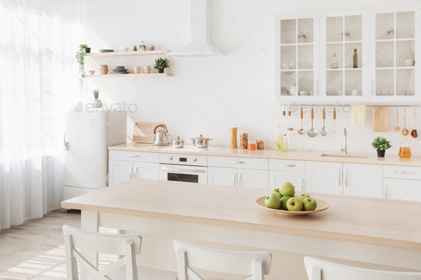 Bright kitchen interior. White furniture and shelves with utensils and plates, small refrigerator