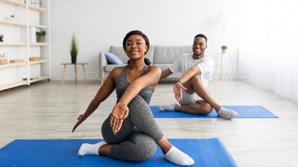 Flexibility exercises for healthier living. Athletic black couple doing yoga  twist pose on home Stock Photo by Prostock-studio