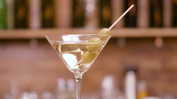Clean Close Up Parallax Shot of a Martini Glass Garnished with Olives alt