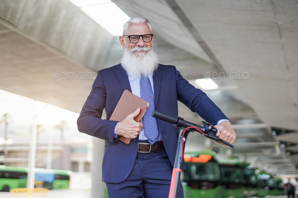 Trendy senior business man at bus station with electirc push scooter