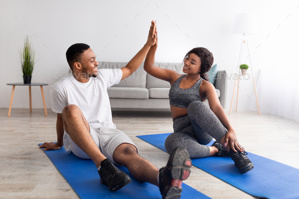 Athletic black guy exercising with his girlfriend on sports mats, giving high five, working out as