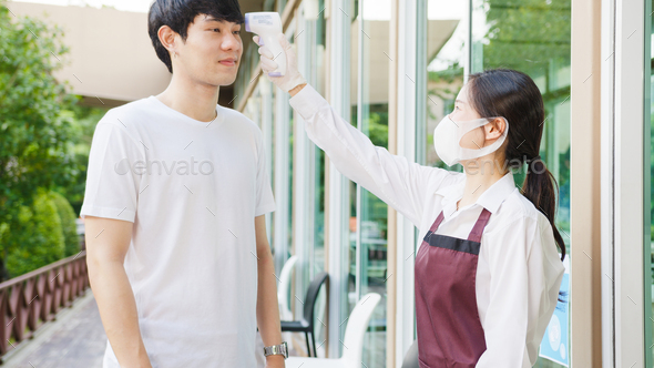Asia female restaurant staff wearing protective face mask using infrared thermometer.