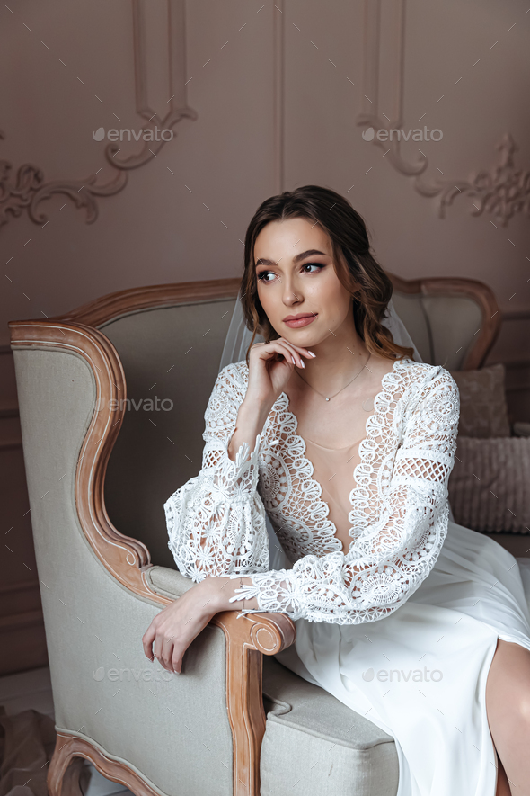 Portrait of a young bride in a chair in a beautiful lace dress.