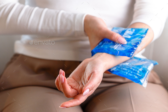 Close up of woman applying cold compress to her painful wrist caused by prolonged work on laptop