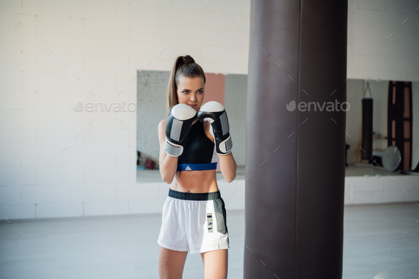 Female kickboxer hitting punching bag while dust particles flies in sunflare light background