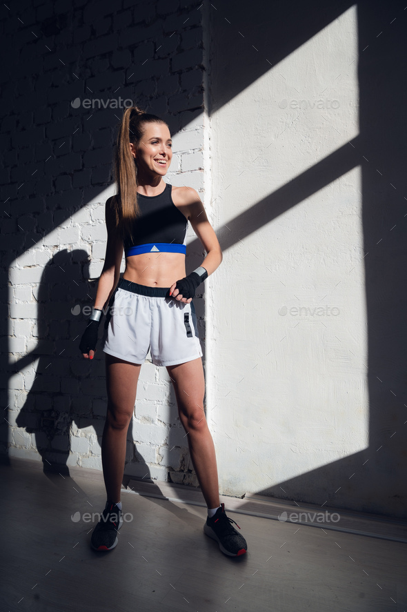 Female kickboxer standing in a boxing studio while dust particles flies in sunflare light background