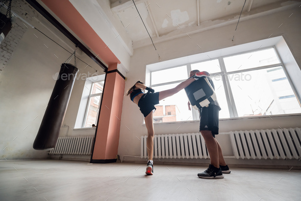 Female martial arts fighter practicing with trainer, punching taekwondo kick pad exercise kicking