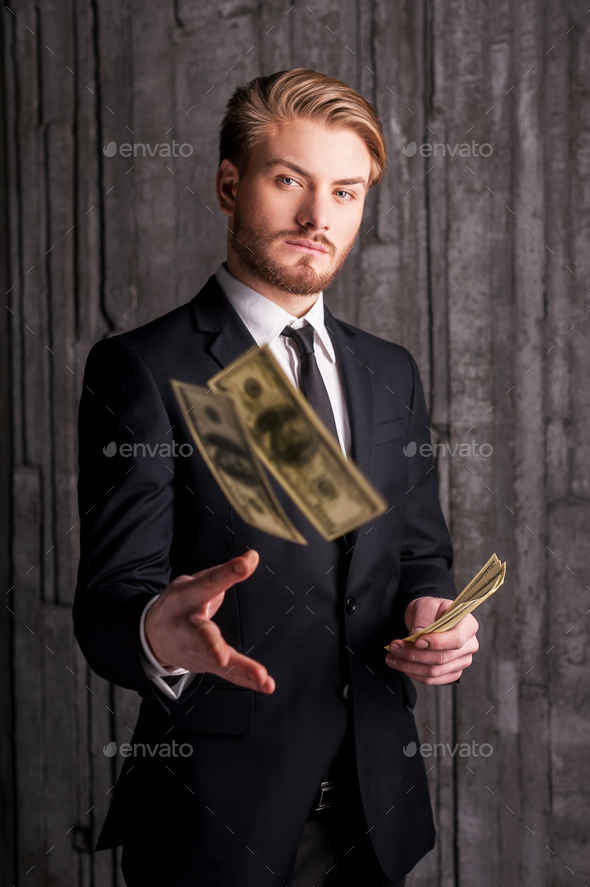 Rich and successful. Handsome young man in formalwear throwing money and looking at camera