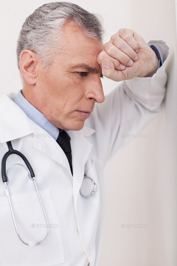 Depressed doctor. Senior grey hair doctor in uniform leaning at the wall and expressing negativity