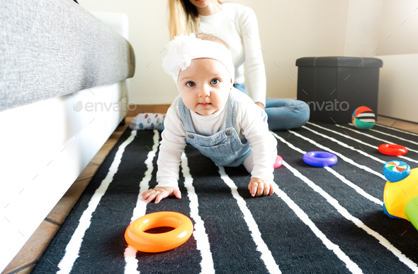Baby girl crawling to grab her toys - New born focusing the camera - Family concept