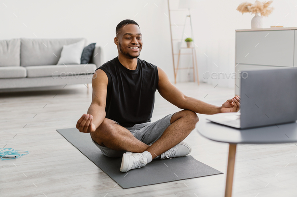 African Man Doing Yoga Online Meditating Sitting At Laptop Indoor