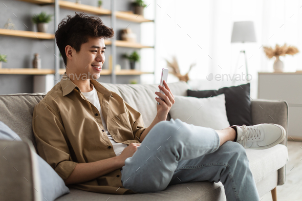Closeup of smiling asian man using smartphone at home
