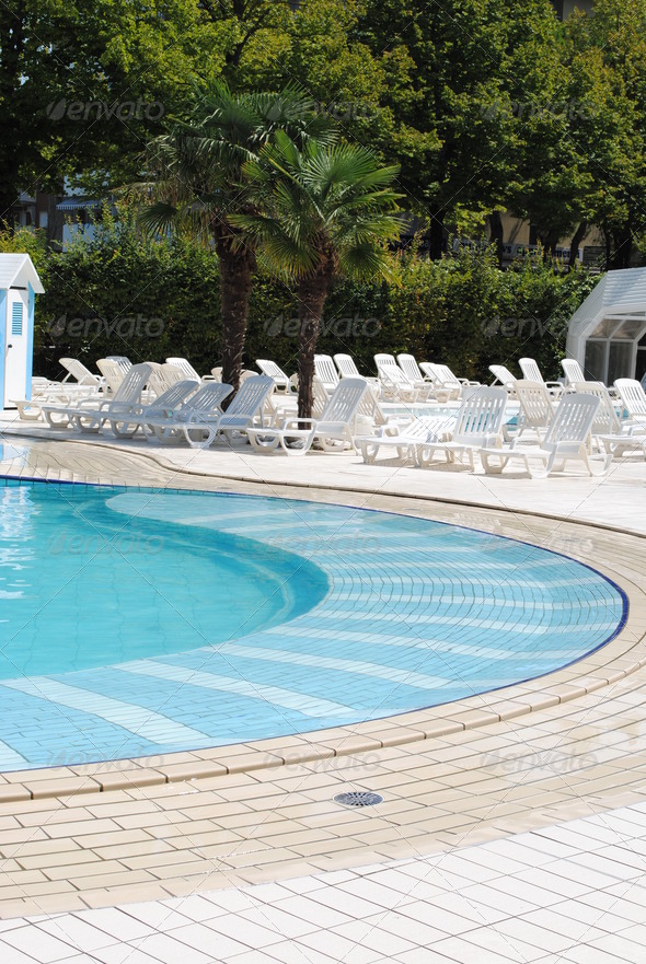 limpid swimming pool and white sunbeds without people
