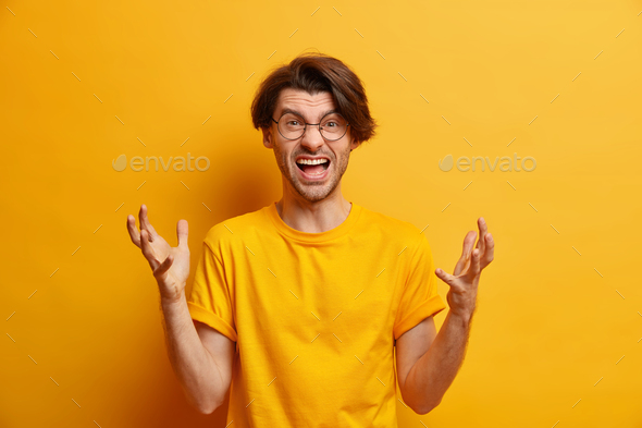 Horizontal shot of peevish angry European man gestures actively exclaims from anger yells with frust - Stock Photo - Images