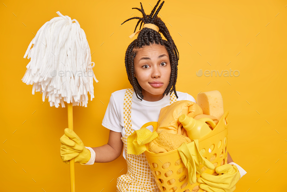 Homework cleaning routine concept. Puzzed Afro American woman with dreadlocks has housekeeping job h