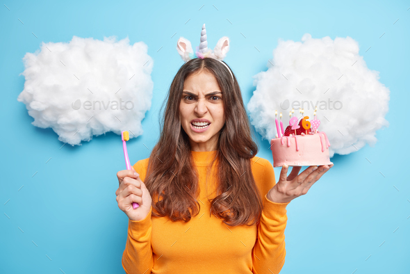 Annoyed displeased brunette woman smirks face holds delicious strawberry cake and toothbrush has car