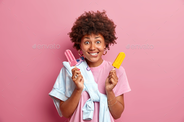Pretty woman with curly hair bites lips cannot wait until eating delicious appetizing ice cream has