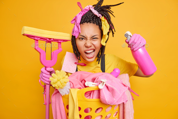 Irritated adult woman with dreadlocks smirks face looks annoyed holds spray detergent to disinfect r