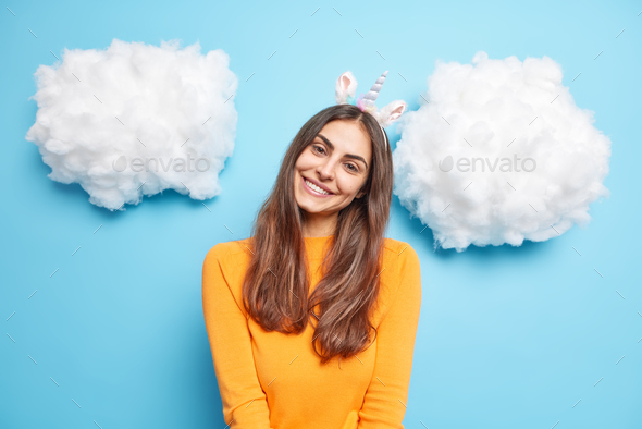Lovely charming woman with long dark hair tilts head smiles gently wears unicorn headband long sleev - Stock Photo - Images