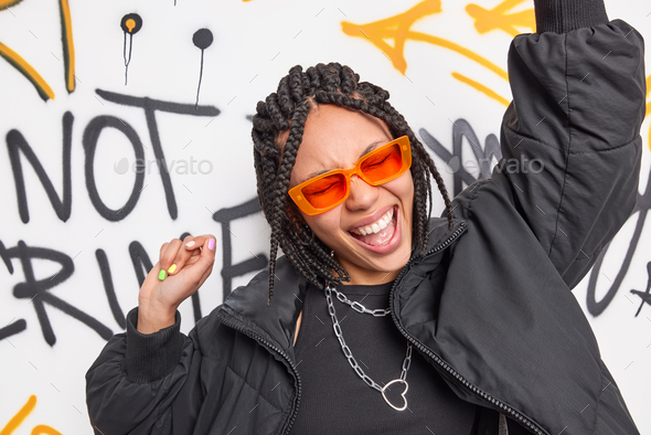Hipster teen girl dances to pop music raises arms has fun sings song wears trendy orange sunglasses