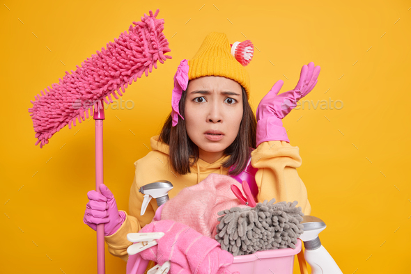 Disappointed busy housewife being angry with children who make mess in house holds mop does laundry