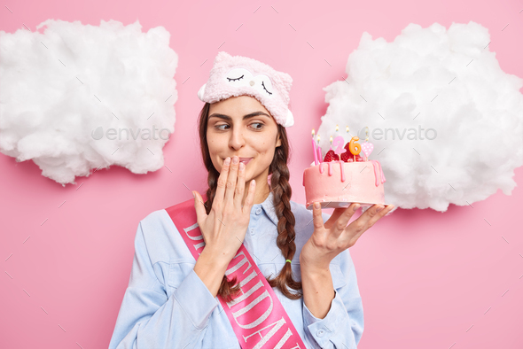 Happy surprised European woman looks with temptation at delicious cake covers mouth waits for guests