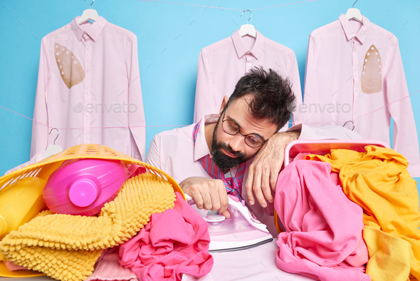 Stressed overworked European man leans at basket of laundry feels exhausted of doing housework uses