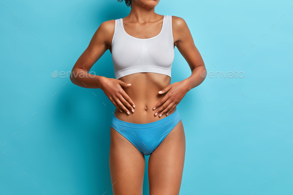 Studio shot of unrecognizable woman has dark skin touches flat stomach poses fit dressed in cropped