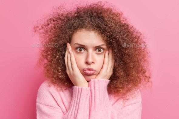 Surprised Curly Haired Young European Woman Keeps Hands On Cheeks