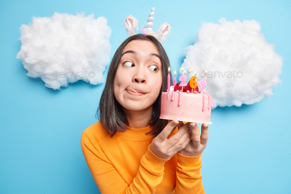 Image of beautiful young Asian woman licks lips looks with temptation at tasty birthday cake going t
