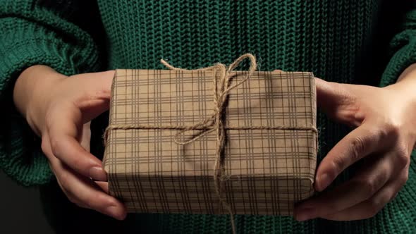 Girl  hand holding a gift wrapped in striped brown paper tied with a rope