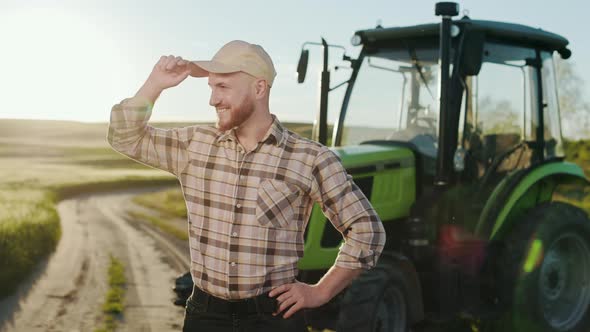 A Young Bearded Farmer is Putting on a Cap and Keeping His Hands on His Belt alt